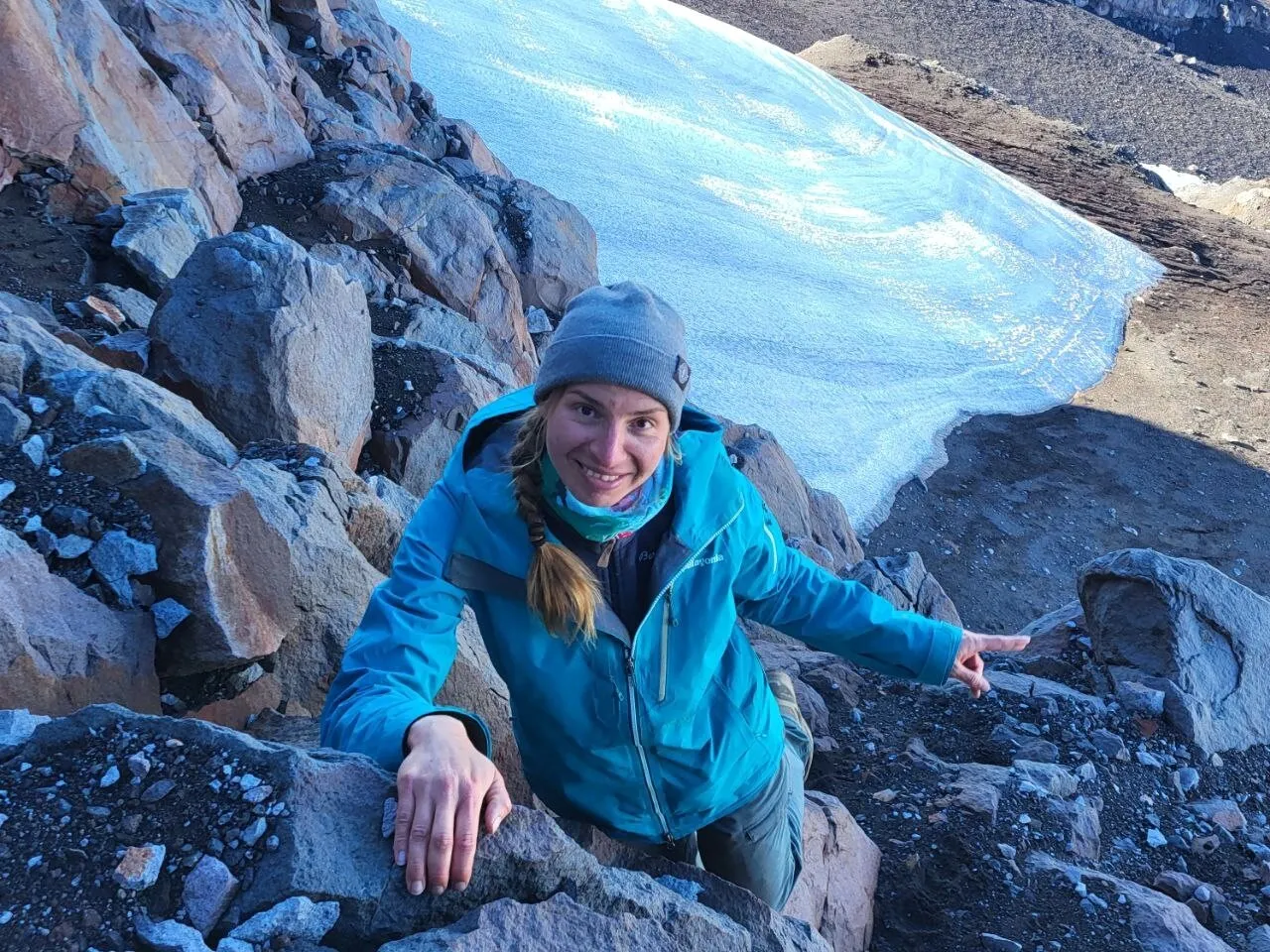 Climber scrambling over rocks beside a snowfield on Calbuco